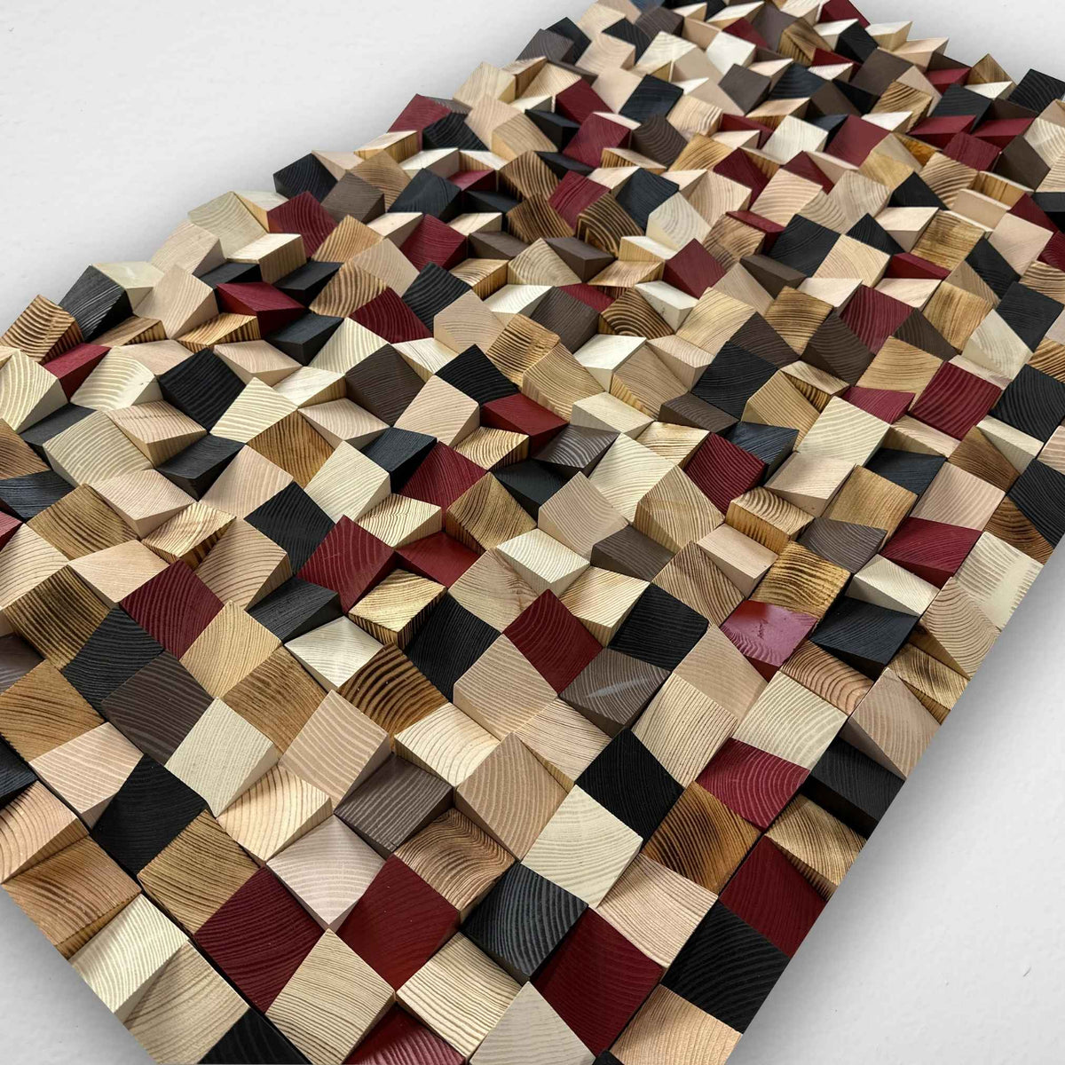 A rectangular wooden wall art panel featuring a 3D geometric pattern of interlocking wooden cubes in various natural wood tones, including beige, brown, black, and dark red, displayed on a light gray background.
