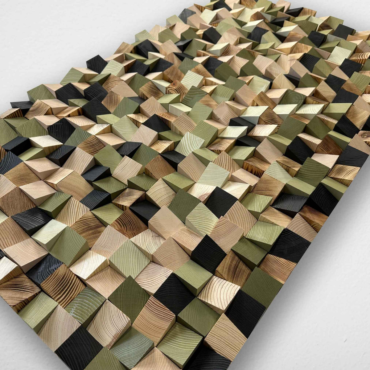 A rectangular wooden wall art panel featuring a 3D geometric design made of raised diamond-shaped blocks in various natural wood tones, olive greens, and black, photographed from an elevated angle on a light gray background.