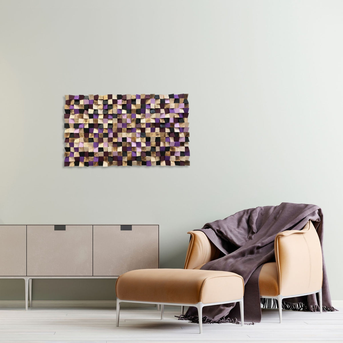 A modern living room scene featuring a rectangular wall art piece with a mosaic pattern of purple, black, and beige tiles, hanging on a light gray wall above a tan armchair, matching ottoman, and a beige sideboard.