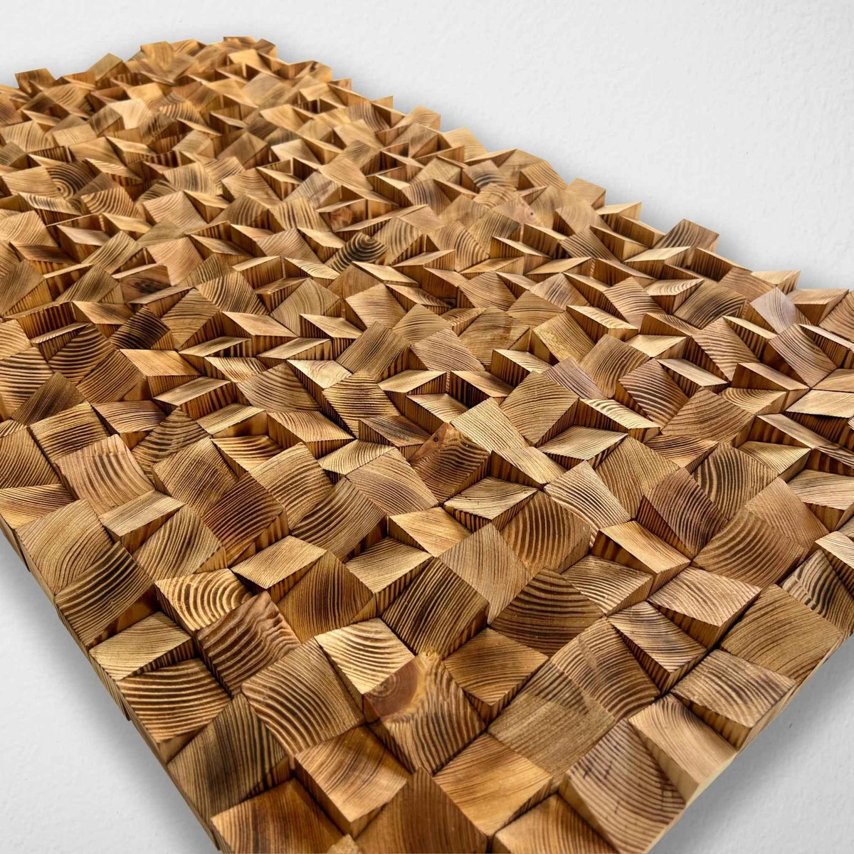 A rectangular wooden wall art panel with a 3D geometric design of interlocking triangular wood blocks, showcasing natural wood grain patterns, photographed against a plain white wall.