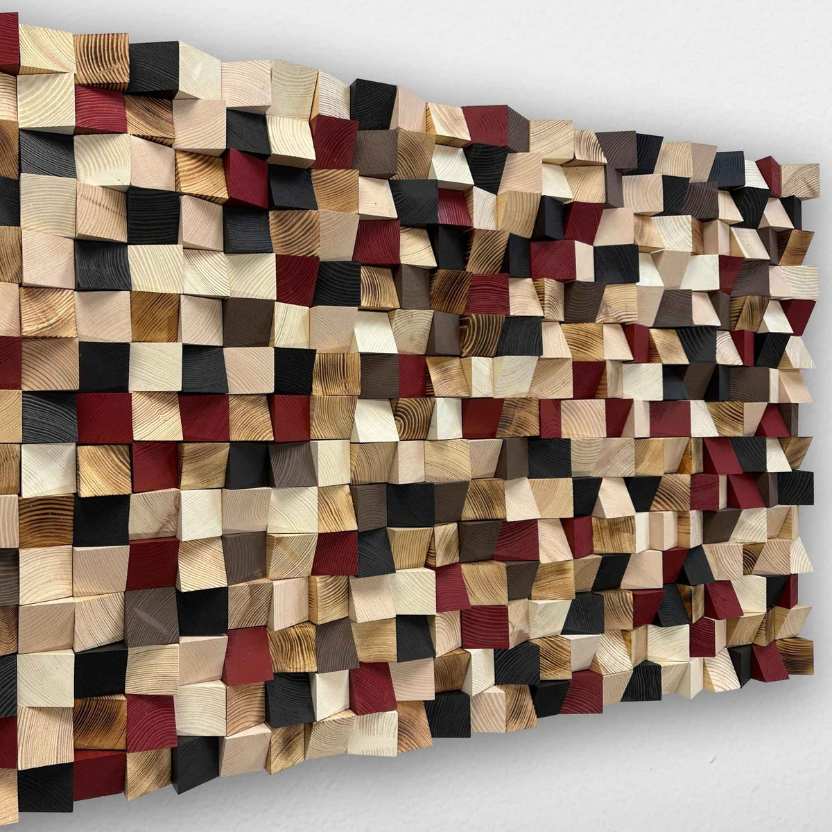 A rectangular wooden wall art panel made of many small square wood blocks in mixed natural tones, including beige, brown, black, and dark red, mounted against a plain light wall.